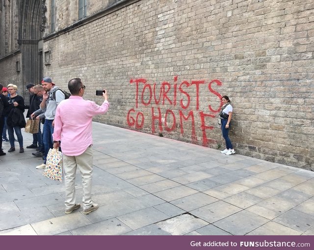 Tourists taking a picture in front of a "Tourists go home" graffiti in Barcelona