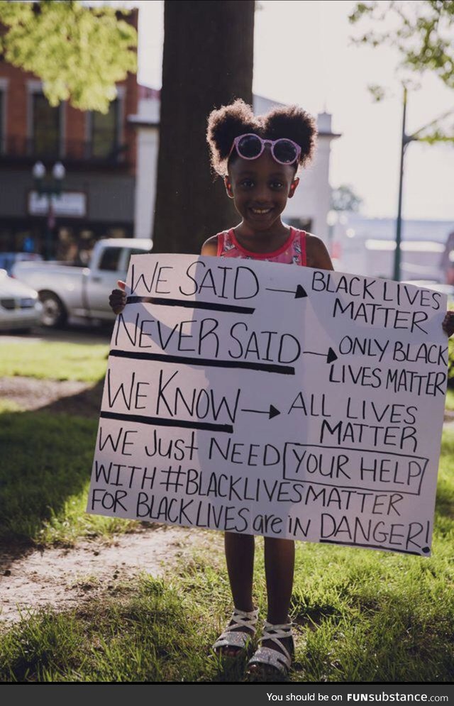 A young girl holding a sign to help explain Black Lives Matter to those who say All Lives