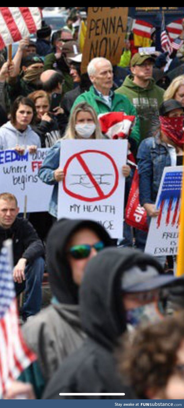 Anti stay at home protester holding an anti mask sign while wearing mask in crowd