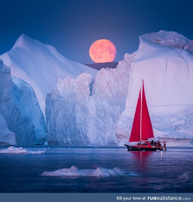 A sailboat passing under a blood moon in Greenland