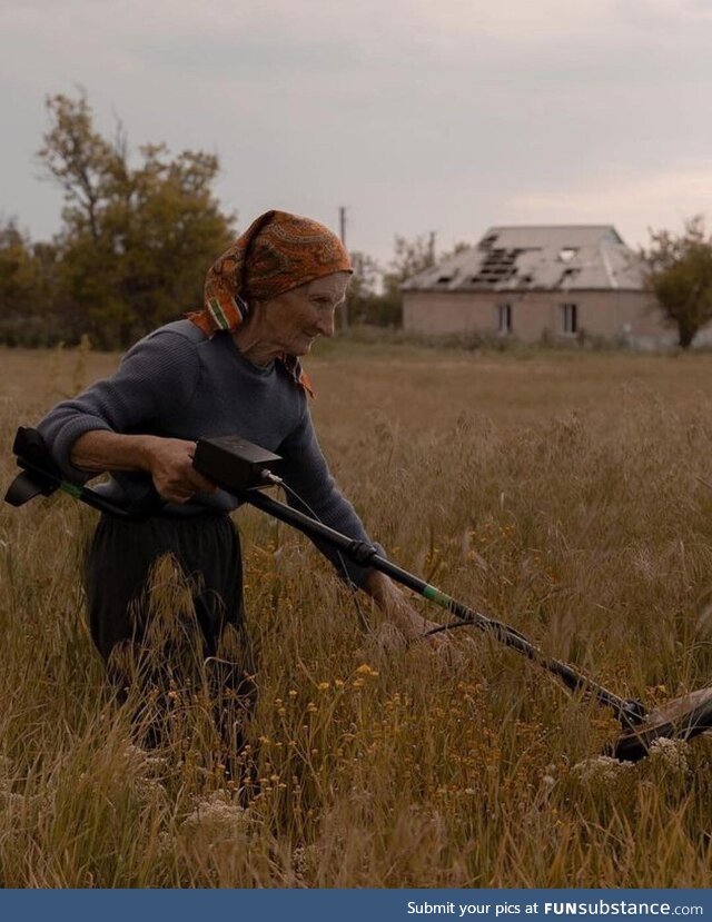 A Ukrainian woman, using a metal detector, is searching for mines on her farm