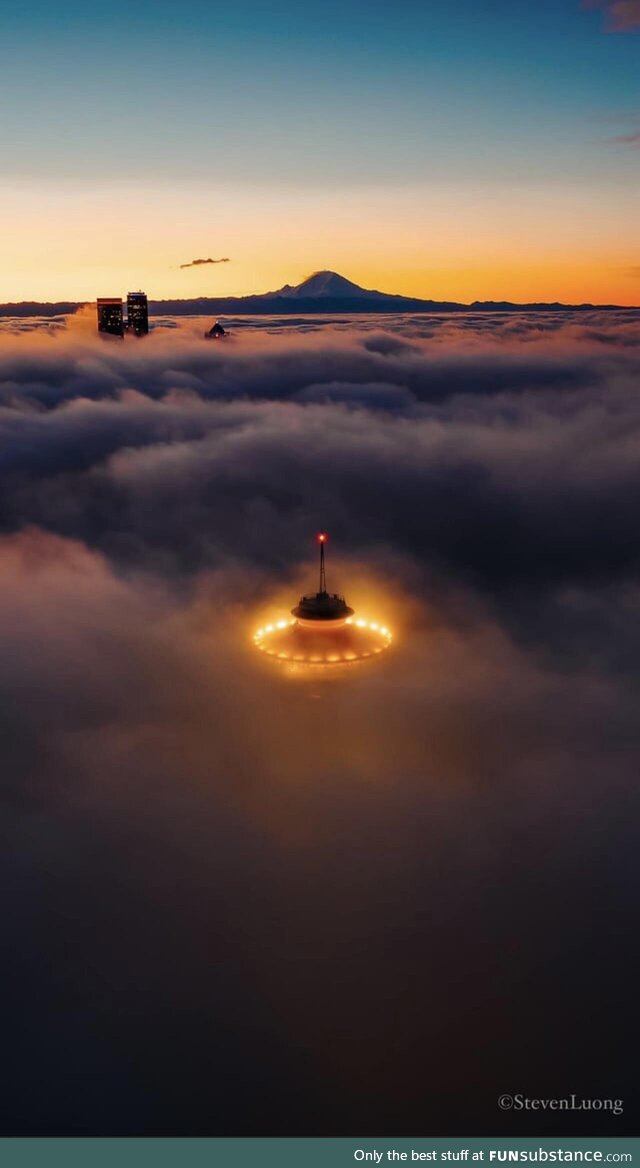 Seattle Space Needle lights shine through the fog with Mt Rainier in the background by