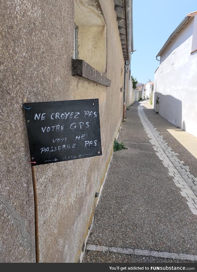 This sign reading "Don't believe your GPS, you can't fit through here" on a tiny street