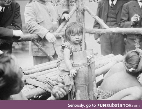 1906 photo of a young Filipino girl sitting on a wooden bench in a human zoo enclosure in