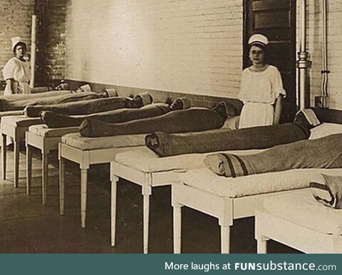 Nurses standing with mentally ill patients wrapped in wet linens. Thought to be calming