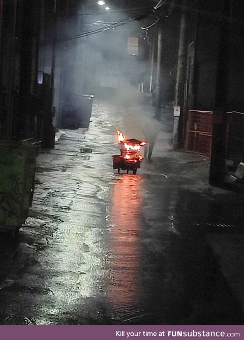 Man pushing a flaming shopping cart down an alley